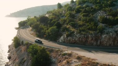 Çatıda kürek çeken araba açık mavi gökyüzünün altında dar bir kıyı yolu boyunca ilerliyor.