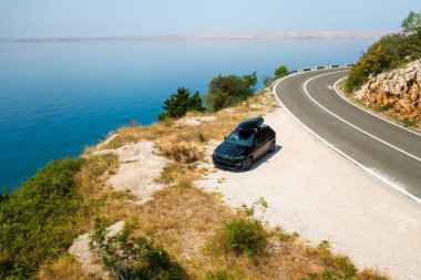  Çatısı olan bir araba uçurumun kenarında duruyor ve arka planda güzel kayalar var..