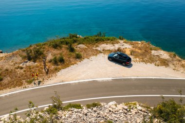 Çatı kutulu bir araba, engebeli bir uçurum yolunun yanında, aşağısı gök mavisi kayalarla çevrili.