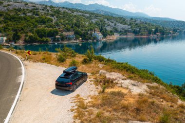 Gök mavisi denize karşı uçurumun kenarında park edilmiş bir araba. Turistlerin Hırvatistan gezisi sırasında deniz manzarasına hayran kalmaları için uygun bir yol kenarı noktası