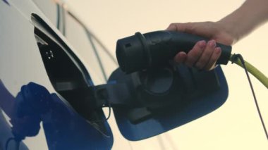 Kadın sürücü şarj etmek için elektrik prizine kablo bağlıyor. Küresel ısınma sırasında çevreyi korumak için elektrik enerjisi kullanımı