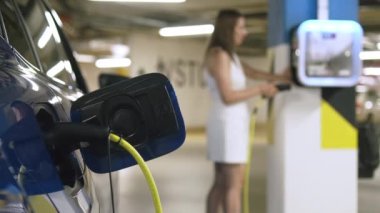 Kadın, elektrik kablosunu otoparktaki bir noktaya bağlıyor. Sürücülerin konforu için modern sürdürülebilir ücret bölgelerinin gösterimi