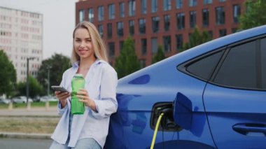 Depoda doldurulabilir su şişesi ve cep telefonu şarjı olan genç bir kadın. Kadın elektrikli araba sahibi modern teknoloji ve sürdürülebilir yaşam gösteriyor