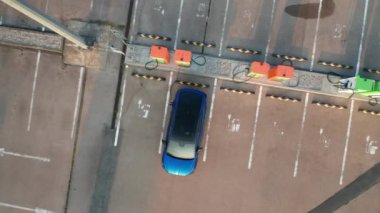 Mavi elektrikli araba otoparkta elektrik alıyor ve şarj istasyonu yukarıdan görünüyor. Modern çevre dostu otomobil, düşük maliyetli yakıtın yararını ortaya çıkardı