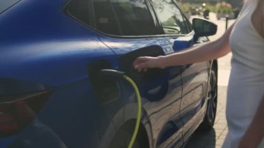 Açık hava şarj istasyonunda elektrik prizinden elektrik kablosu çıkaran kadın sorunu. Kadın kabloyu sökmek için çabalıyor.
