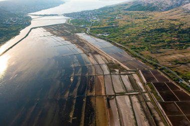 Gün batımında tuzlu tavaların hava görüntüsü deniz suyu buharlaşması ve tuz üretimini gösteriyor.