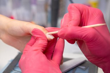 Manikür ustasının bir güzellik salonunda pembe eldivenli turuncu çubuk uygulaması.. 