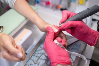 Pembe eldivenli en iyi manikür teknisyeni güzellik salonunda bir kadının parmak uçlarında tırnak matkabıyla ustalıkla manikür yapıyor.