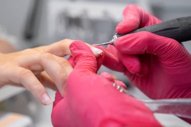 Pembe eldivenli manikürcü bir güzellik salonunda manikür yapıyor.