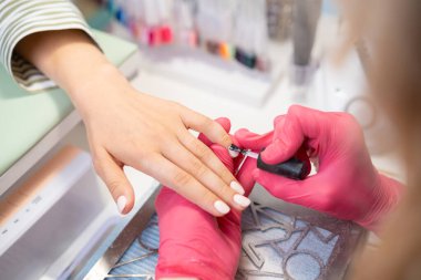 Pembe eldivenli bir manikürcü müşterilere kusursuz bir son vermek için jel cilası sürüyor..