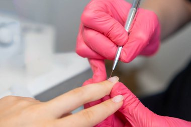 Pembe eldivenli manikürcü güzellik salonunda bir taban jeli cilası tabakasını düzeltmek için küçük bir fırça kullanıyor.