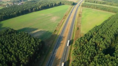 Arabalar ve kamyonlar otoban boyunca otlarla çevrili araziler ve ormanlarla birlikte hareket ediyorlar. Yol tarlalardan ve sık yeşil orman alanlarından uzanıyor.