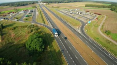 Dev kamyon römorku, dört şeritli otoban için yamaç kenarındaki park alanından ayrılıyor. Düzgün bir şekilde park edilmiş büyük kamyonlarla dolu otopark.