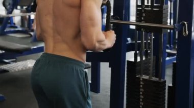 Athlete performs muscle strengthening exercise by sport equipment. Young man does chest pull-down on large cable machine in spacious gym