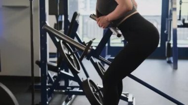 Bayan spor salonunda kemer sırasına dizilmiş halteri kullanıyor. Deri giyen bir kadın sırt kaslarını izole etmeye çalışır. Sırt kasları çok az gerilir.