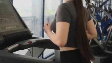Sporcu kadın koşu bandında koşup geniş spor salonundaki monitörlere bakıyor. Spor giyimli genç bir kadın baldırlarını ve kalçalarını geliştiriyor ve dayanıklılık artıyor.
