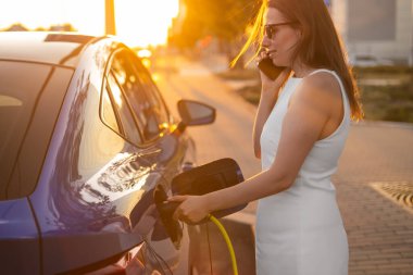 Gün batımında yol kenarında bir telefon görüşmesi yapan bir kadın elektrikli araca şarj oluyor.. 