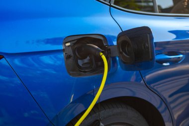 Halka açık bir şarj istasyonunda sarı kabloyla elektrikli bir araca elektrik yüklemek.. 