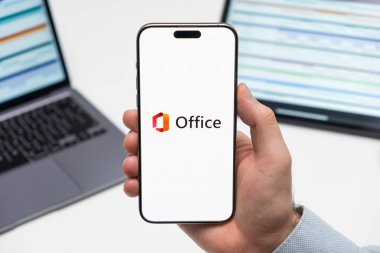 PRAG, CZECHIA - 2024 Temmuz: Microsoft Ofis logosu arka planda erkek eli ve dizüstü bilgisayarda akıllı telefon ekranında 