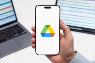 PRAG, CZECHIA - JULY, 2024: Google disk logosu arkaplanda erkek eli ve dizüstü bilgisayarda akıllı telefon ekranında 