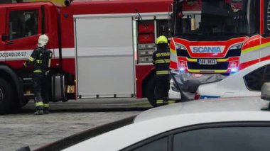 PRAG, CZECH REPUBLIC - 15 Mart 2024: acil durum itfaiyecileri park halindeki kurtarma kamyonunun yanında ekipman hazırlamak için gelir. Üniformalı ekip olay sırasında polis arabasının yanındaki caddede çalışıyor.