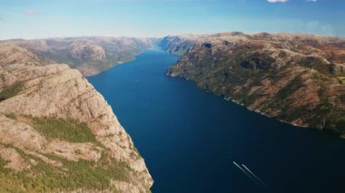 Görkemli Lysefjord engin mavi gökyüzünün altındaki engebeli dağların arasında derin rüzgarlar esiyor. Serin mavi sular Norveç 'teki küçük teknelerle güneş ışığını yansıtıyor