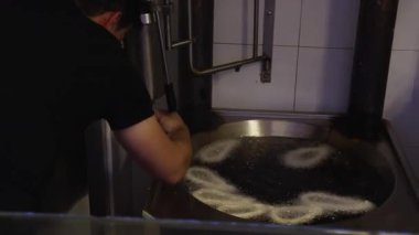 Adam çiğ Churro 'ları elleriyle kaynar yağın içine yerleştiriyor. Petrol baloncukları ve fritöz halka şeklindeki churro spiralleriyle dolarken, hamur lavaboları özel aletlerden içeri giriyor.