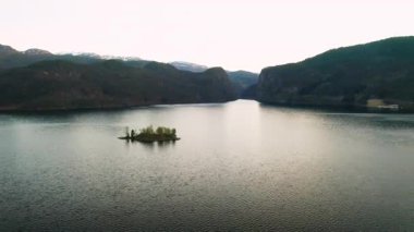 Sakin sulara sahip fiyort, sessiz gökyüzünün ışığını yansıtır ve heybetli dağlarla çevrilidir. Norveç 'te ağaçlarla kaplı küçük bir ada merkezi sularda bulunur.