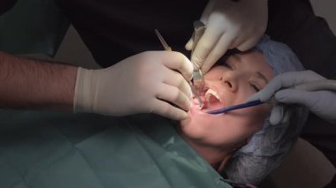 Diş uzmanlarından oluşan bir ekip, hasta ağzı tutma aletleri ve hazırlık alanı üzerinde çalışıyor. Kadın ifadesi prosedür sırasında rahatsızlık anlarını öneriyor
