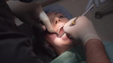 Dişçiler hasta ağız boşluğunda hazırlayıcı prosedürleri gergin bir şekilde gerçekleştirirler. Yüz ifadesi implant hazırlama aşamasında rahatsızlık gösteriyor.