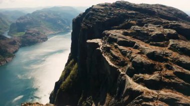 Lysefjord 'un ihtişamı Preikestolen' in egemenliğinde. Uçurumun dik yüzeyi, Norveç 'teki uzak tepelerin ipuçlarıyla birlikte derin mavi fiyordun üzerinde yükseliyor.