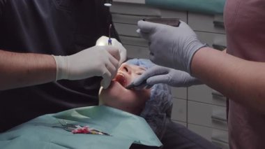 Diş hekimi, kemik grefti malzemesi uygulanırken hasta ağzı üzerinde çalışır. Kadın sandalyede yatarken asistan erişimi sürdürmeye yardımcı olur