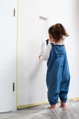 Mutlu kıvırcık saçlı kız daire duvarını silindirle boyamama yardım ediyor.