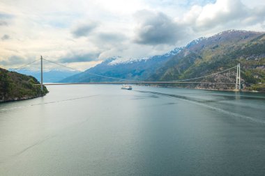 Hardanger Köprüsü fiyort üzerindeki sakin sularda büyük yelkenli yolcu gemisiyle zarifçe kemerlerle dönüyor. Görkemli dağlar Norveç 'in dingin güzelliğini özetliyor