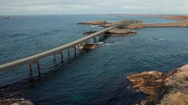 Magnificent stretch of Atlantic ocean road with long bridge gracefully spanning deep blue waters. Rough waves crash near rugged coastline in Norway