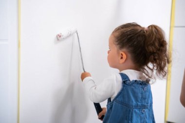 Küçük kız duvarı boyayarak oturma odasını dekore ediyor.