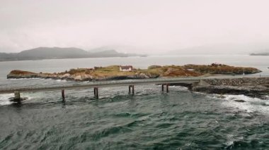 Norveç 'in çalkantılı sularındaki adaları birbirine bağlayan eğimli köprüyle Iconic Atlantic Okyanus Yolu. Engebeli kıyı şeridi ve karamsar gökyüzünün altındaki sisli dağlar