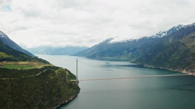 Hardanger Köprüsü, dağların dramatik manzarasıyla çevrili engin fiyortları incelikle kaplar. Uzun ince köprü mimari zarafeti vurguluyor