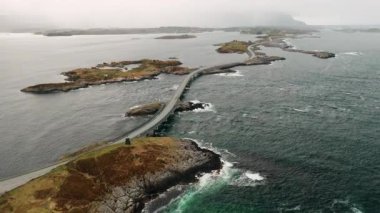 Dönen Atlantik okyanus yolu deniz suyu boyunca küçük kayalık adaları birbirine bağlar. Bulutlu gökyüzü altında Norveç takımadalarından geçen resim gibi bir rota