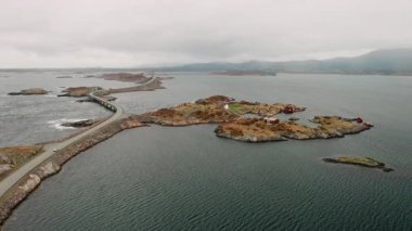 Atlantik Okyanus Yolu 'nun dramatik mühendisliği engebeli adalarda örgü örüyor. Sakin suların arasında bulutlu gökyüzünün altında sisli mesafelere uzanan yollar.