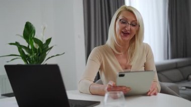 Orta yaşlı sarışın psikolog tabletle hastayla konuşuyor. Bej kıyafetli olgun bir kadın terapist video görüşmesi yapıyor. Modern uzaktan terapi ve akıl sağlığı kavramı.