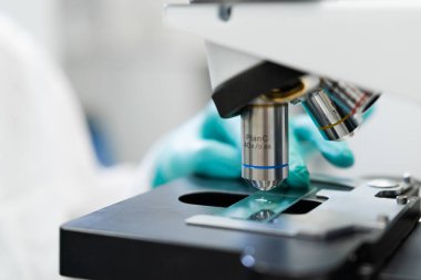 Scientist in laboratory closely examining specimen under microscope.
