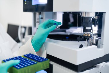 Scientist performing chromatography analysis by inserting vial into automated injection system in laboratory environment.
