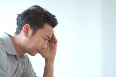 Mutsuz Asyalı genç adam oturma odasında kanepede oturuyor ve ellerini birarada tutuyor. Stresli Asyalı adam oturma odasında tek başına oturuyor. Endişeli ve endişeli bir adam.