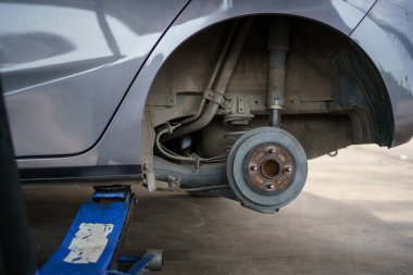 Hidrolik kriko kullanan teknisyen ya da tamirci arka tekerleği değiştirmek için arabayı kaldırır..