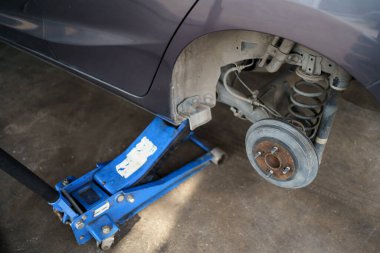 Hidrolik kriko kullanan teknisyen ya da tamirci arka tekerleği değiştirmek için arabayı kaldırır..