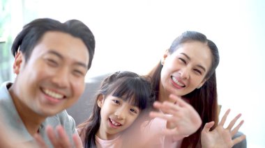 Mutlu Asyalı aile, baba, anne ve kız oturma odasında birlikte yaşıyorlar. Ebeveynler güzel kızlarıyla birlikte akıllı telefondan selfie çekiyorlar..