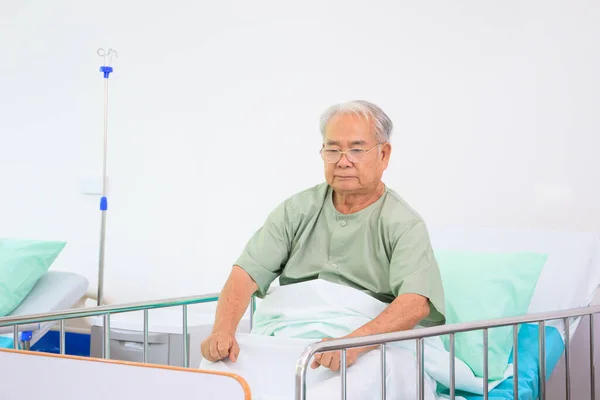 Elder Asian man in nursing home sitting on the bed alone. Lonely Asian old man sitting and vacant looking for something. Mental health care - mental wellbeing in elder people concept.