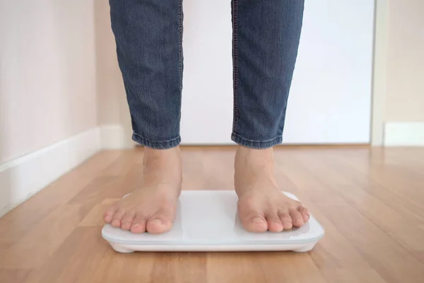 Unrecognizable woman stepping on the digital display weighting scale to measure her body weight and overall body mass index. Health care and wellbeing concept in modern people.