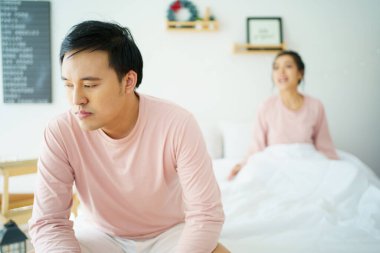 Mutsuz, stresli Asyalı bir adam karısı ona bağırırken yatakta oturuyor. Karı koca arasında ailevi bir sorun hakkında ciddi ya da kritik tartışmalar..